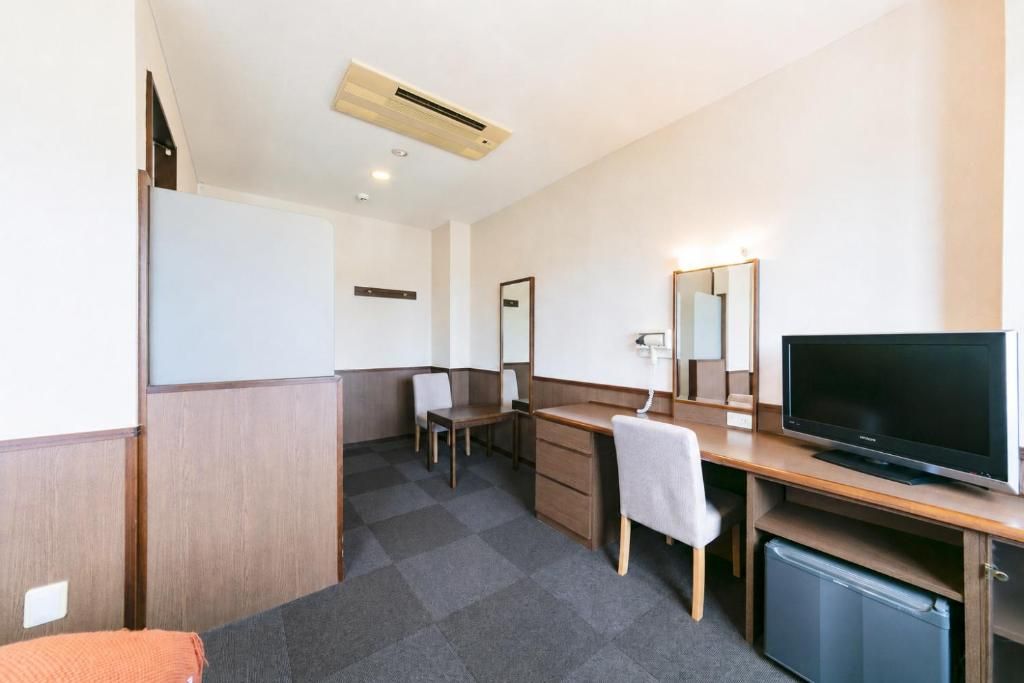 Habitación de hotel con cama, escritorio, silla, televisor y un refrigerador pequeño.