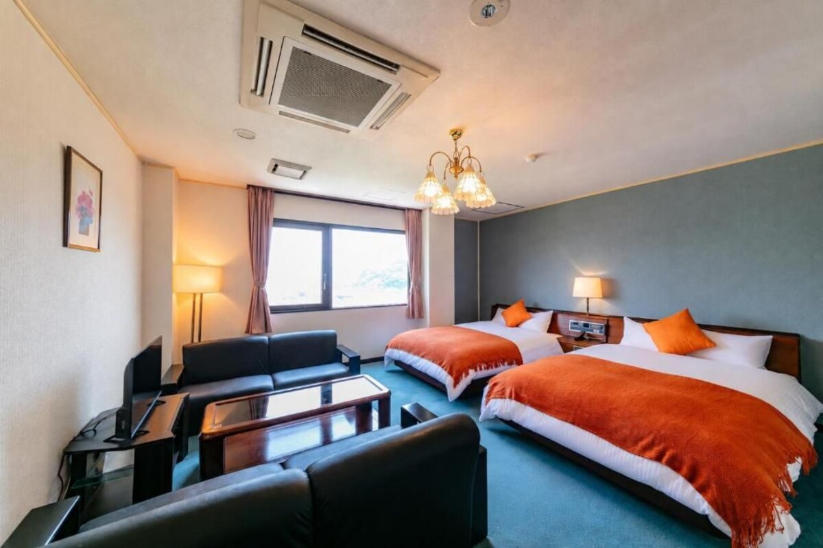 A hotel room with two beds, a desk, a chair, a lamp, and a window.