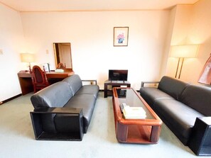 A hotel room with two black leather sofas, a wooden coffee table, a TV, and a desk with a lamp. - Mango Hotel Nichinan (Nichinan City Iwasaki)