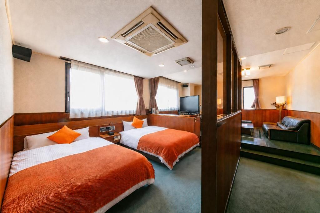 A hotel room with two beds, a television, a desk, and a sofa.