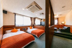 A hotel room with two beds, a television, a desk, and a sofa.