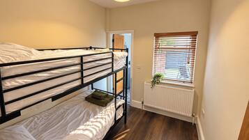 Ein Schlafsaalzimmer mit Etagenbetten, einem Heizkörper, einem Fenster mit Jalousien und einer Pendelleuchte.