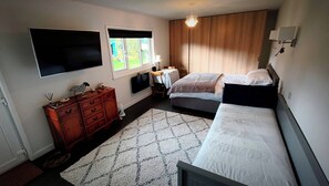 A bedroom with two beds, a dresser, a TV, a window, and a chandelier.