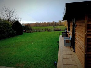 A wooden deck with outdoor seating, a grassy yard, and a view of a field.