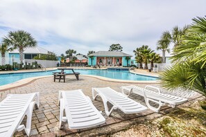 Una piscina con sillones de descanso y una mesa de picnic, rodeada de palmeras y edificios.