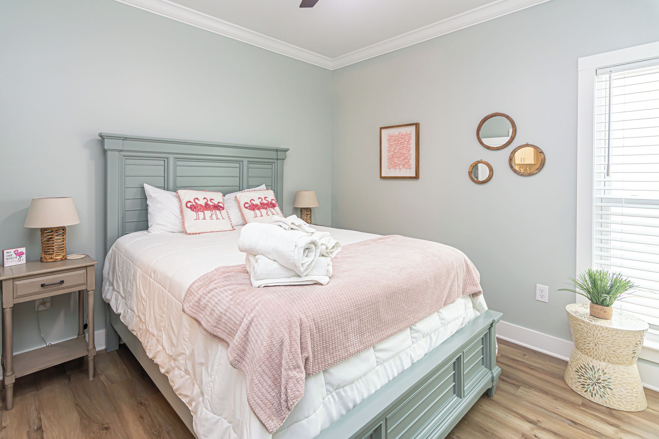 Un dormitorio con cama, mesitas de noche, un espejo en la pared y una ventana con persianas.