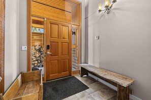 A wooden door with a handle, a bench, and a wall-mounted light fixture in a hallway. - Big White is Calling - Full House with Hot Tub (Kootenay Boundary)