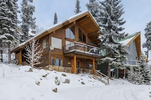 A wooden cabin with a balcony, surrounded by snow-covered trees. - Big White is Calling - Full House with Hot Tub (Kootenay Boundary)