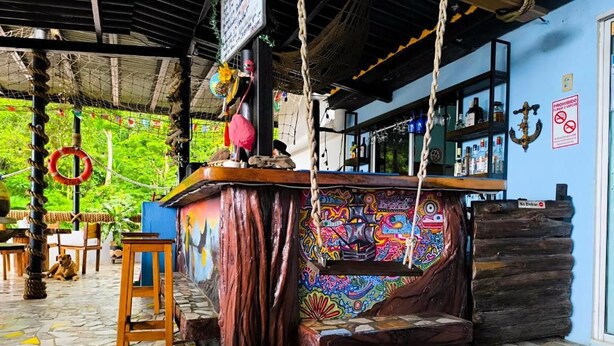 A bar area with a colorful mural, wooden logs, and a stone-tiled floor.