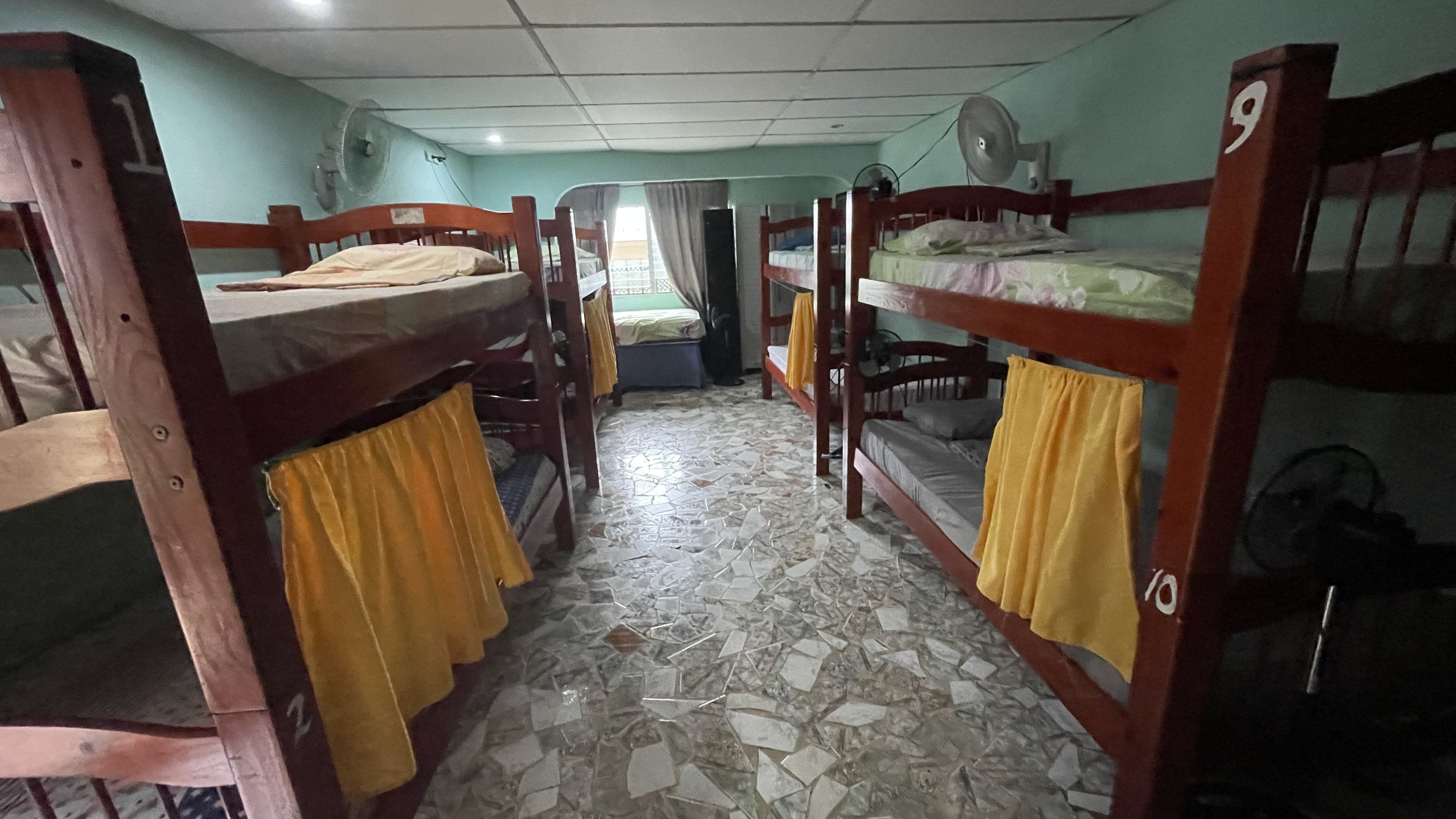 Une chambre de dortoir avec des lits superposés, un sol carrelé et un ventilateur au plafond.