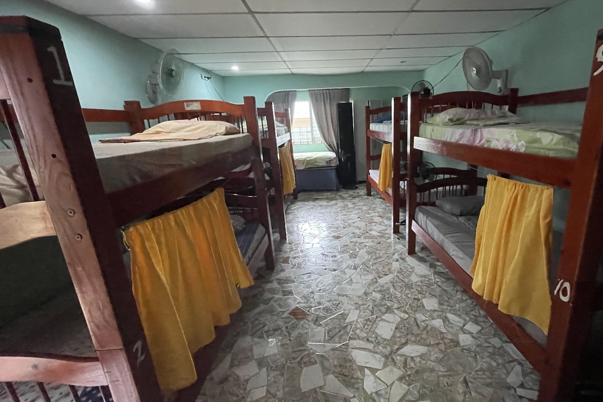 A dormitory room with bunk beds, a tiled floor, and a ceiling fan.