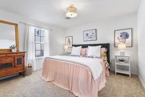 Quarto com cama, penteadeira, mesas de cabeceira e espelho.