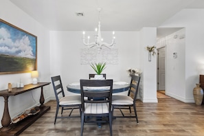 A dining area with a round table, four chairs, a chandelier, a painting, and a vase with flowers. - Furnished Executive Stay Offers 2 Living, 2 King 1 Queen Private Primary Suite (Tulsa)