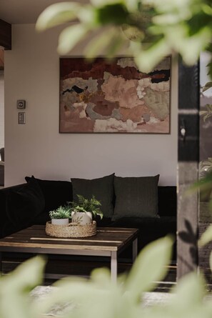 Ein modernes Wohnzimmer mit einem dunklen Sofa, einem Couchtisch mit Pflanze und einem großen abstrakten Gemälde an der Wand.