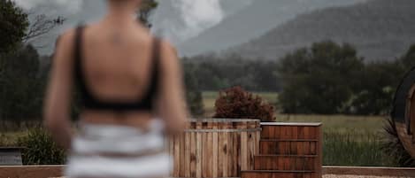 Une personne se tient dans un jardin, près d’une structure en bois, avec une vue sur les montagnes.