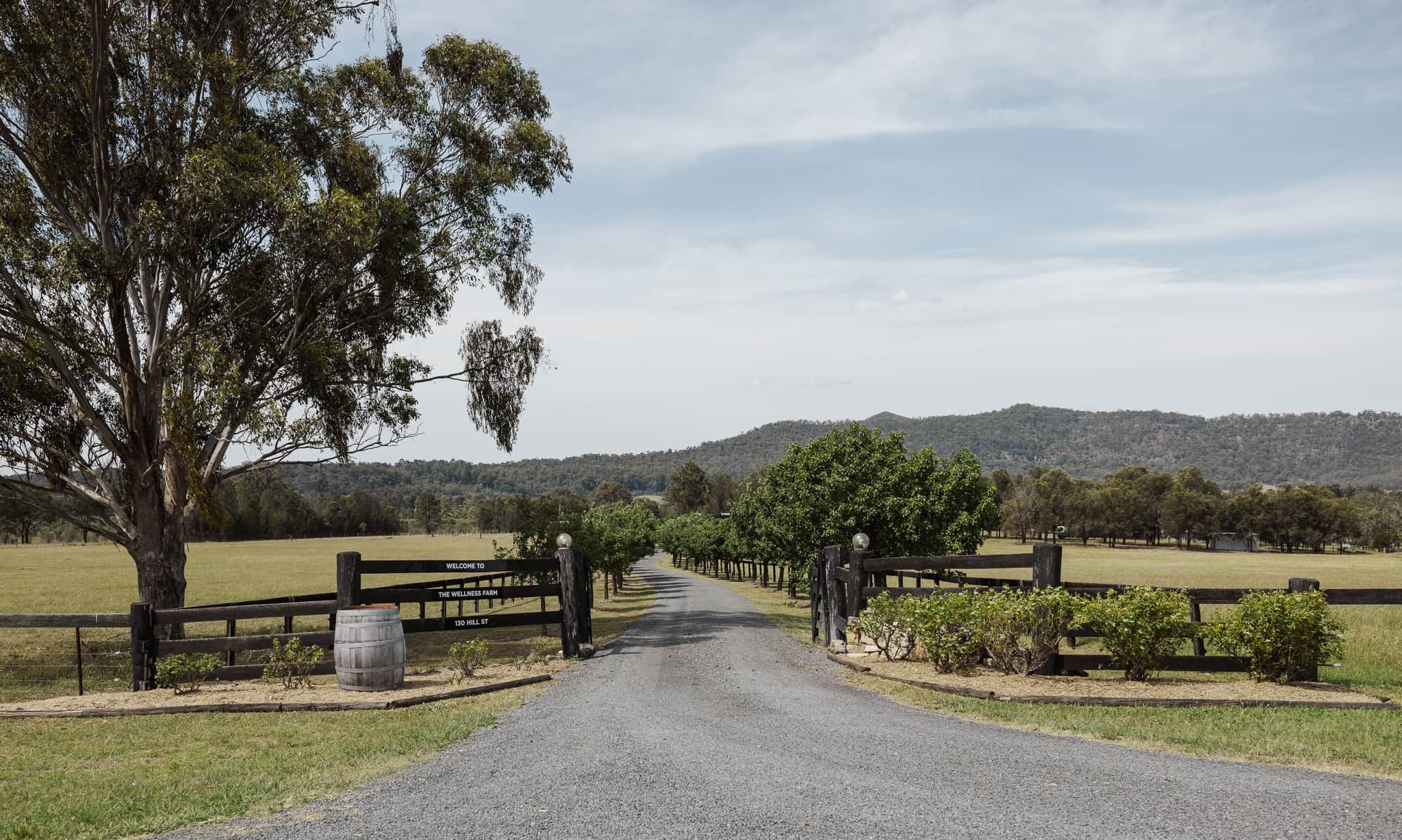 A rural road leading to a farm with a wooden fence and a welcome sign.
