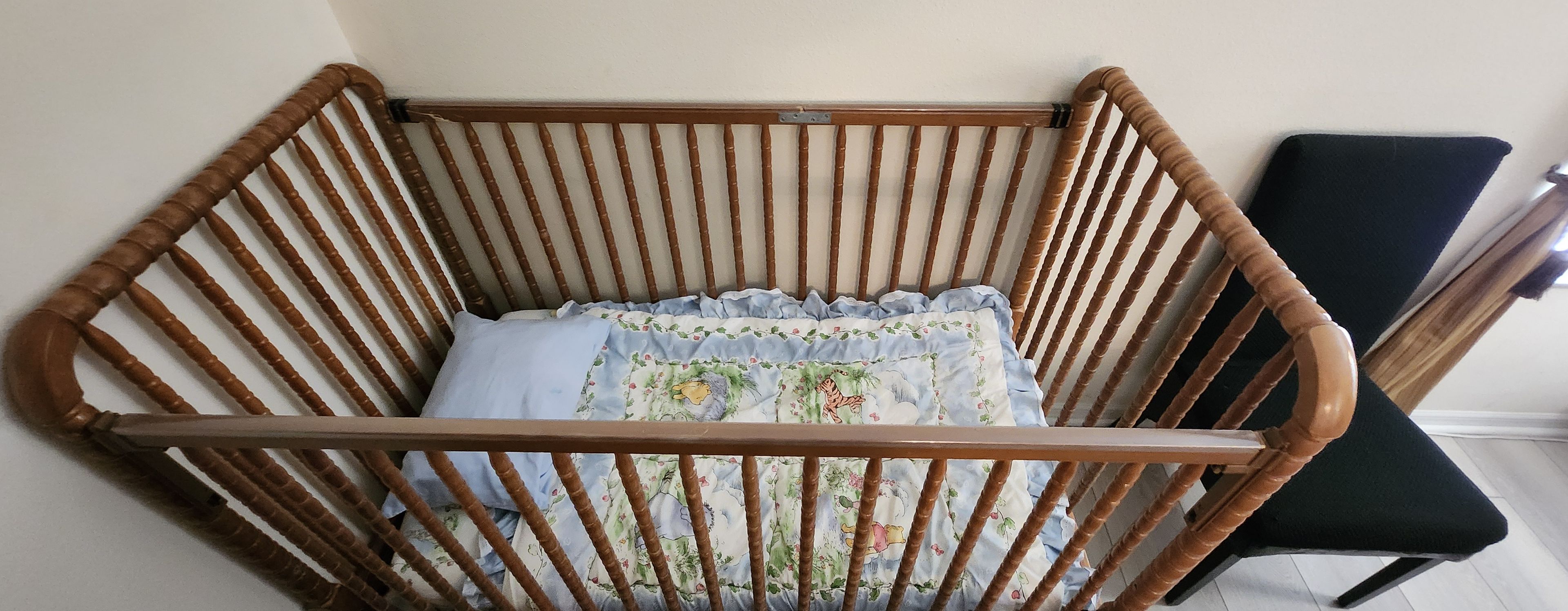 Una cuna de madera con un cojín floral y una silla negra al fondo.