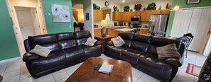 Ein Wohnzimmer mit zwei schwarzen Ledersofas, einem Holztisch und einer Küche im Hintergrund.