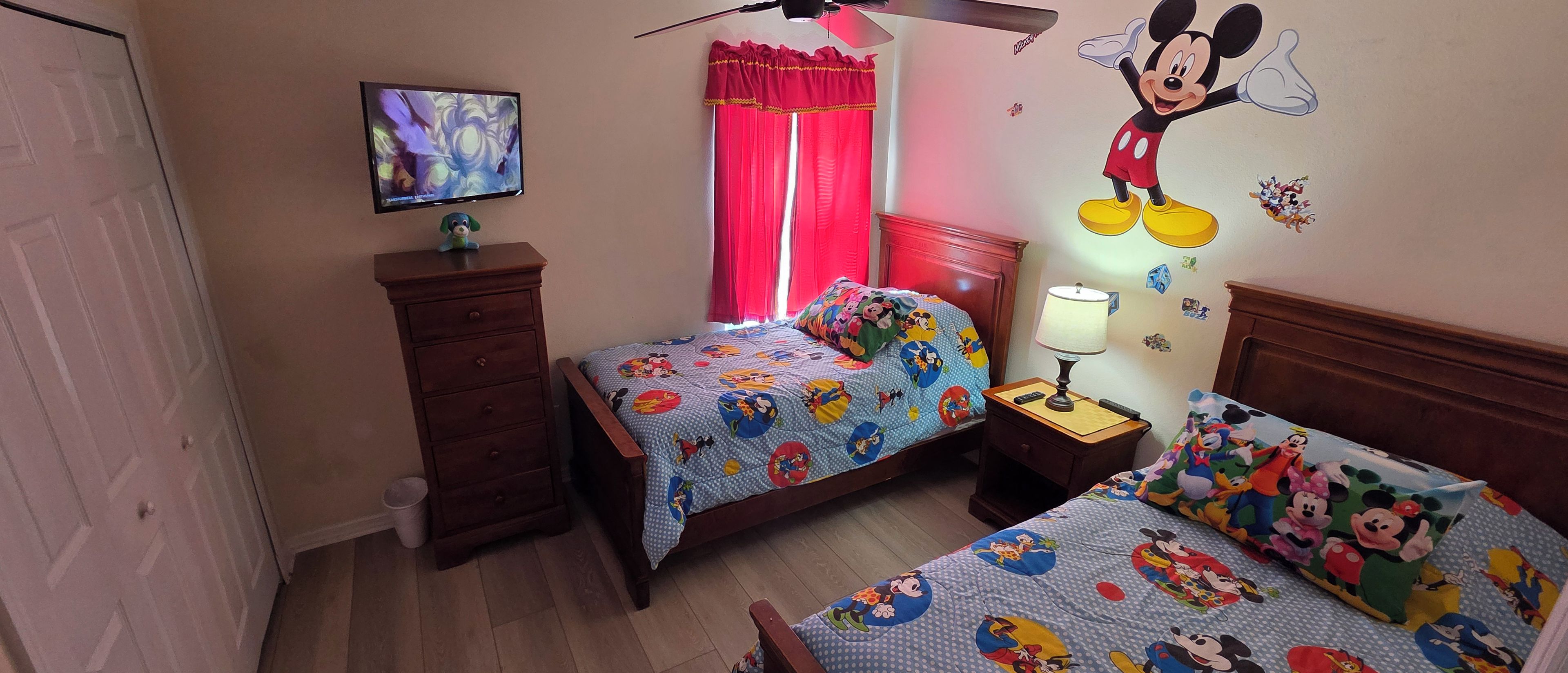 A child's bedroom with two beds, a TV, and a Mickey Mouse wall decal.
