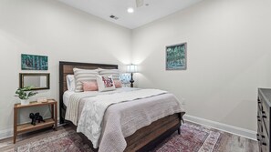 A bedroom with a bed, bedside table, lamp, and artwork on the walls. - Crimson Cajun | Where Southern Comfort Meets Football (Tuscaloosa)