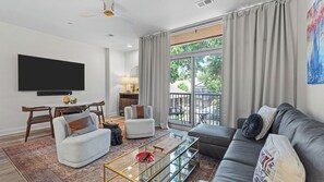 Ein Wohnzimmer mit Flachbildfernseher, einer Couch, Sesseln, einem Couchtisch und einem Essbereich mit Tisch und Stühlen.