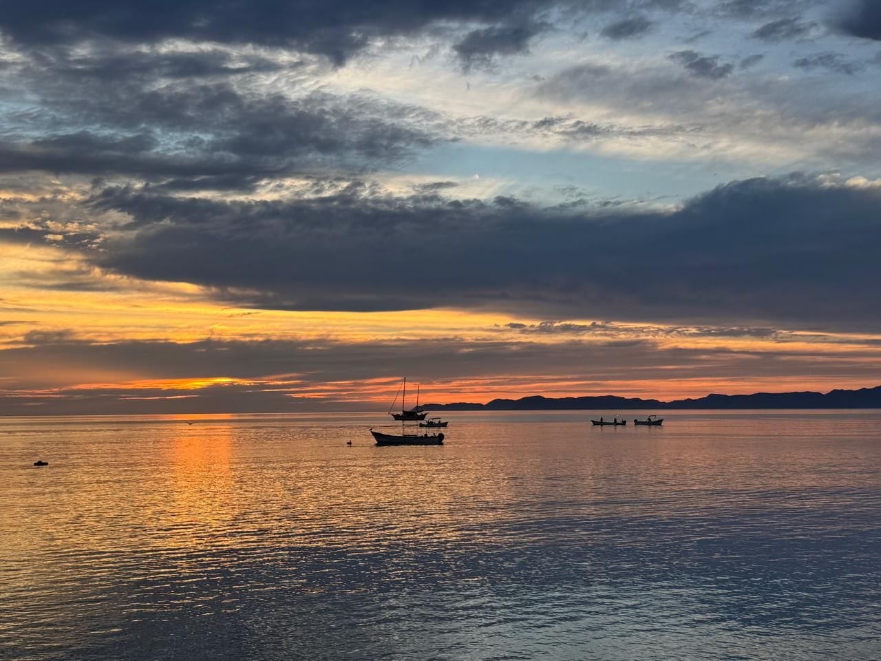 A calm body of water with boats and a sunset in the background.