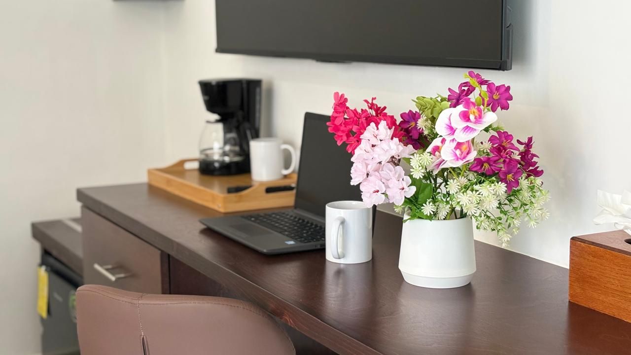 A desk with a laptop, a coffee maker, a mug, and a vase of flowers.