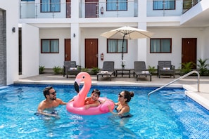 A swimming pool with a pink flamingo float, lounge chairs, and a building with balconies in the background. - HOTEL THE Q (Loreto)