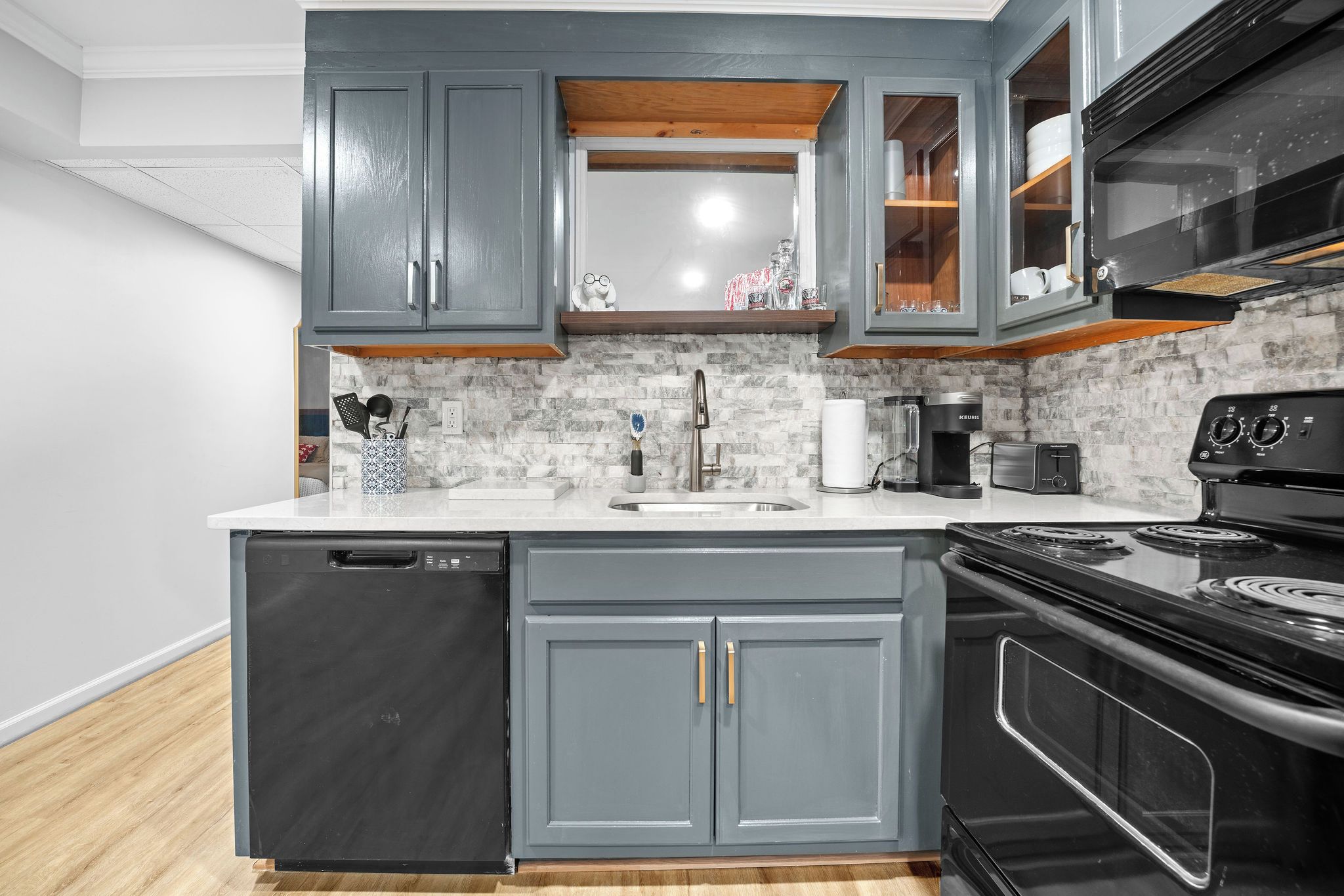 A kitchen with grey cabinets, a black dishwasher, a stove, and a microwave.