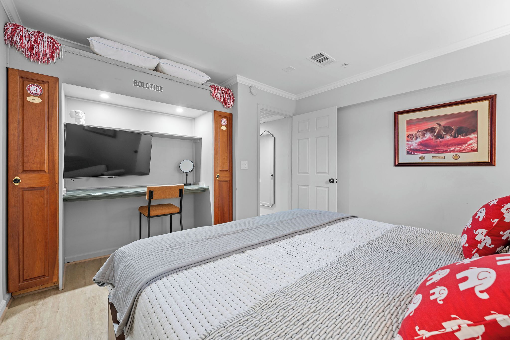 A bedroom with a bed, a desk, a chair, a mirror, and a framed picture on the wall.