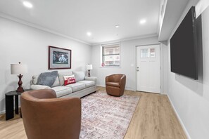 A modern living room with a sofa, armchair, and a flat-screen TV mounted on the wall. - Legacy Retreat | Walk to Bryant-Denny (Tuscaloosa)