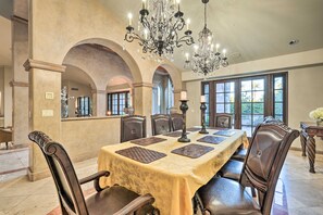 Ein Esszimmer mit einem langen Tisch, Stühlen, Kronleuchtern und großen Fenstern.