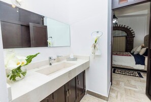 Une salle de bain avec un lavabo blanc, un miroir et un vase rempli de fleurs blanches.