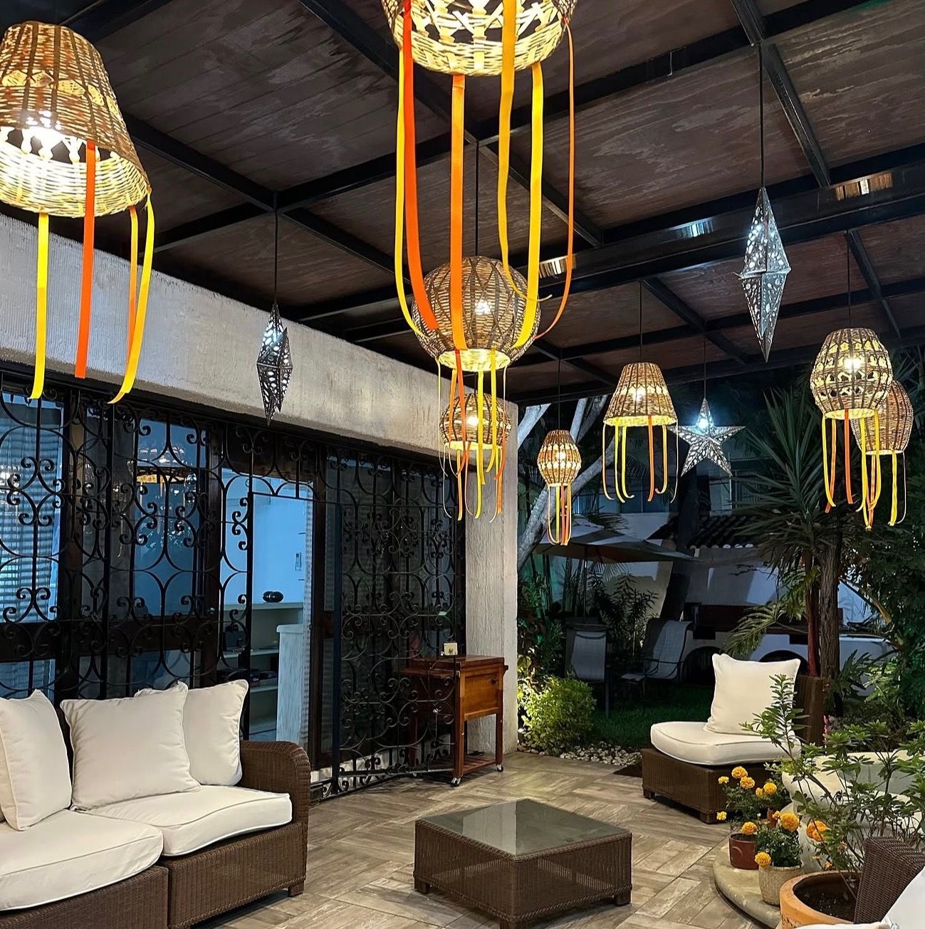 A lounge area with wicker furniture, hanging lanterns, and a view of the outdoors.