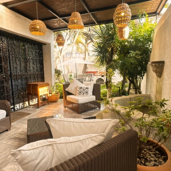 Un espace extérieur aménagé, abrité et doté de mobilier en osier, de luminaires suspendus et de plantes en pot.