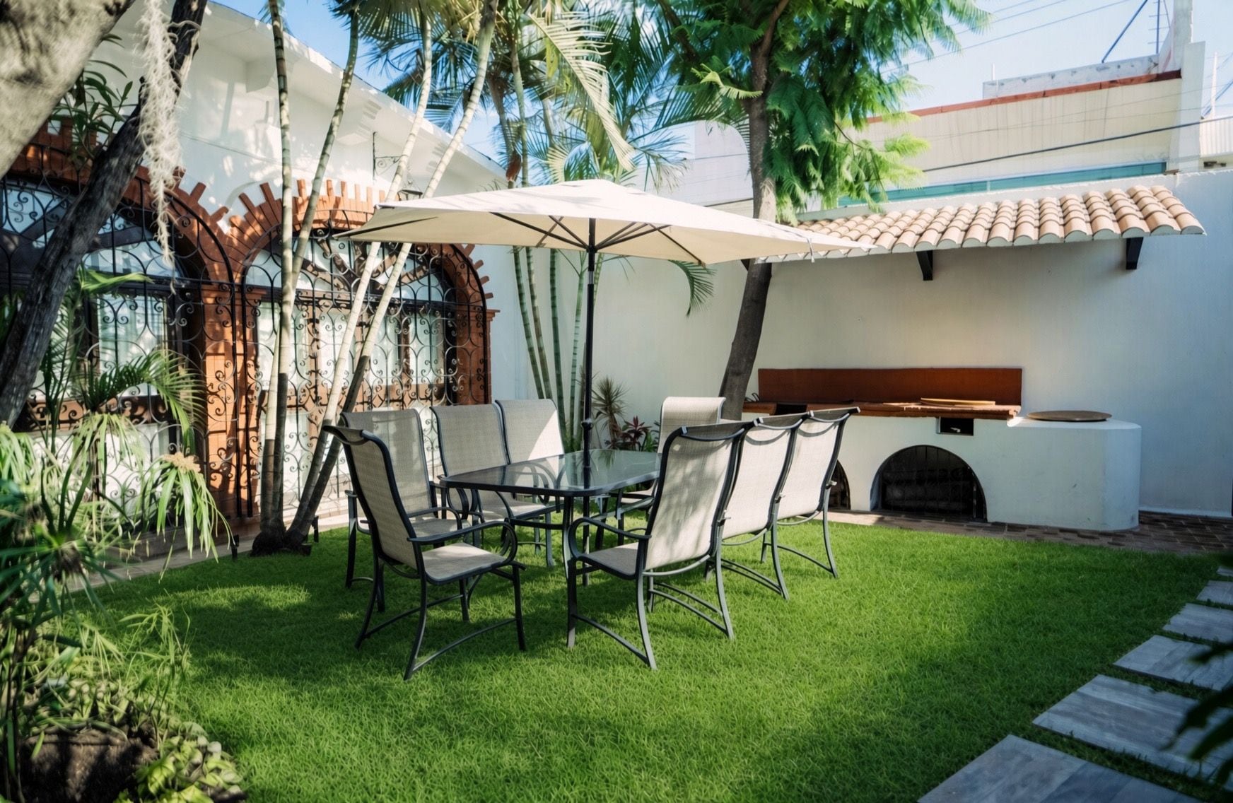 Eine Terrasse im Freien mit Tisch und Stühlen, einem Grill und einer weißen Wand mit einem Ziegeldach.
