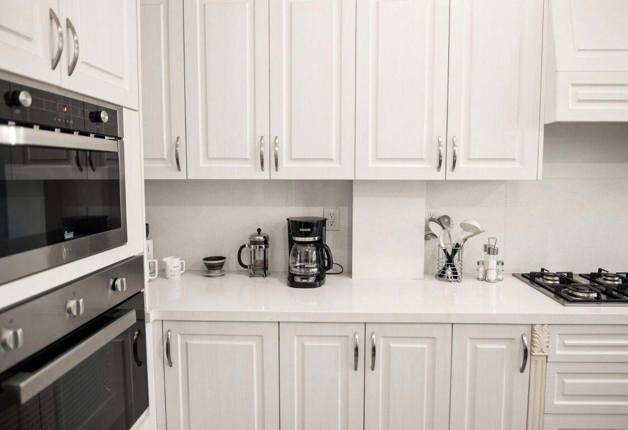 A kitchen with white cabinets, a stove, a coffee maker, and a microwave.