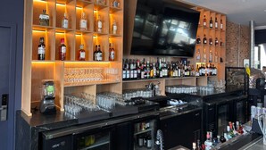 Zona de bar con estantes llenos de botellas de licor, un televisor y una barra con vasos y una licuadora.