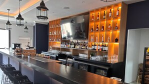Zona de bar con una barra larga, varias estanterías llenas de botellas, un televisor y taburetes.