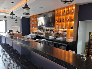 Un espace bar doté d’un long comptoir, de plusieurs étagères remplies de bouteilles, d’un téléviseur et de tabourets de bar.