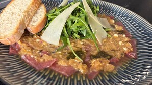 Un plato de comida con pan y vegetales verdes, una copa de bebida oscura, y una lata de refresco en un bar.