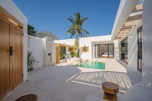 A modern outdoor pool area with a palm tree, a wooden deck, and a white building with large windows. - Palmera Moana Uluwatu (Pecatu)