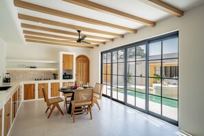 A modern kitchen with wooden beams, a dining area with a large window overlooking a pool. - Palmera Moana Uluwatu (Pecatu)
