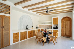 A modern kitchen with wooden cabinets, a dining table with chairs, and a ceiling fan. - Palmera Moana Uluwatu (Pecatu)