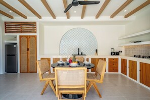 A modern kitchen with a dining area, featuring wooden furniture, a large island, and a ceiling fan. - Palmera Moana Uluwatu (Pecatu)