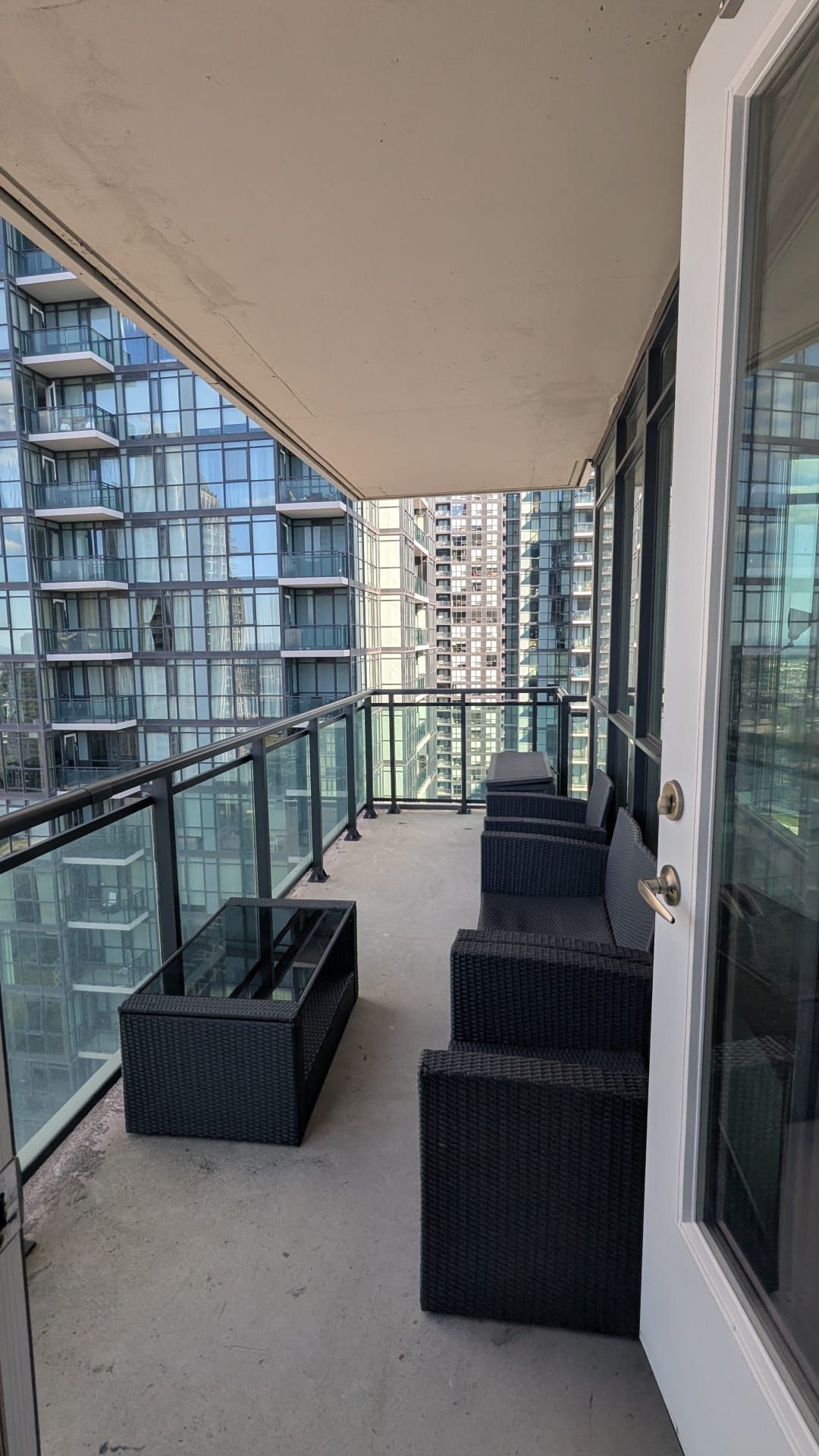 A balcony with wicker furniture, glass railings, and a view of high-rise buildings.
