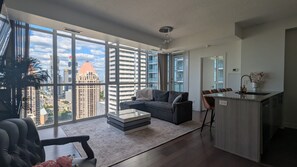 A modern living room with a sofa, a coffee table, and a view of a cityscape through large windows.