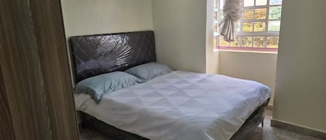 A bedroom with a bed, a window with curtains, and a painting on the wall.