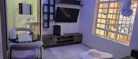 Una sala de estar con televisor de pantalla plana, un sofá, una mesita, una silla y un ventanal con vistas.