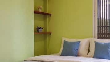 A room with a bed, a window with blinds, and a shelf with decorative items.